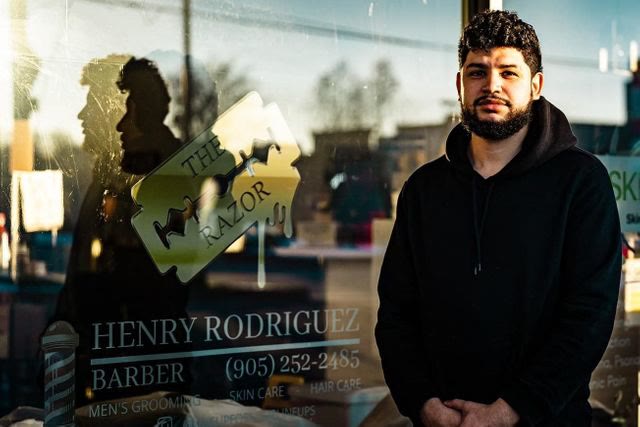 Henry Rodriguez standing outside his shop window, with The Razor logo and his name on the glass